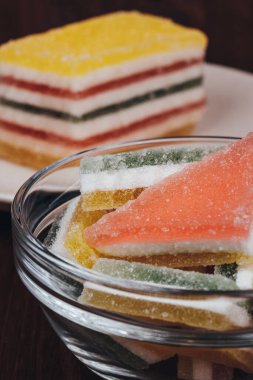 Colorful jelly candy in the plate and glass bowl on wooden background. Multi-colored marmalade jelly candy's. Heap of triangular and rectangular  marmalade candy. Macro shot, selective focus.