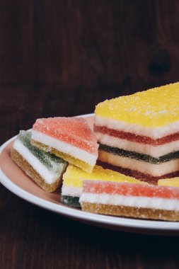 Ahşap arka plandaki tabakta renkli jöle şekeri. Çok renkli marmelatlı reçelli şekerler. Bir yığın üçgen ve dikdörtgen marmelat şekeri.