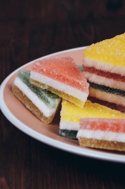 Ahşap arka plandaki tabakta renkli jöle şekeri. Çok renkli marmelatlı reçelli şekerler. Bir yığın üçgen ve dikdörtgen marmelat şekeri.