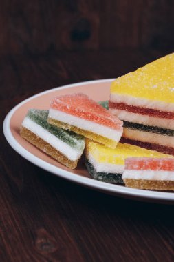 Ahşap arka plandaki tabakta renkli jöle şekeri. Çok renkli marmelatlı reçelli şekerler. Bir yığın üçgen ve dikdörtgen marmelat şekeri.