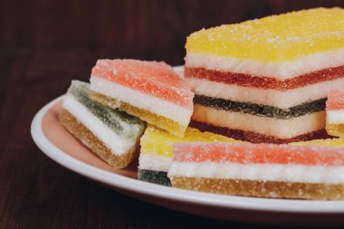 Ahşap arka plandaki tabakta renkli jöle şekeri. Çok renkli marmelatlı reçelli şekerler. Bir yığın üçgen ve dikdörtgen marmelat şekeri.