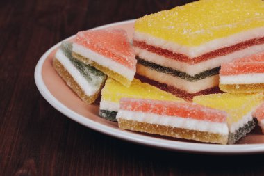 Ahşap arka plandaki tabakta renkli jöle şekeri. Çok renkli marmelatlı reçelli şekerler. Bir yığın üçgen ve dikdörtgen marmelat şekeri.