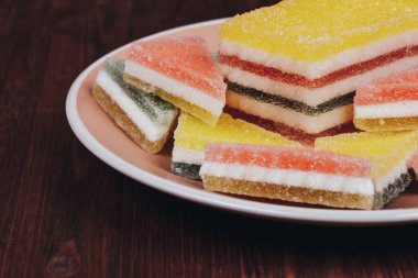 Ahşap arka plandaki tabakta renkli jöle şekeri. Çok renkli marmelatlı reçelli şekerler. Bir yığın üçgen ve dikdörtgen marmelat şekeri.