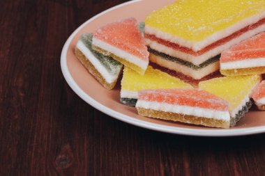 Ahşap arka plandaki tabakta renkli jöle şekeri. Çok renkli marmelatlı reçelli şekerler. Bir yığın üçgen ve dikdörtgen marmelat şekeri.