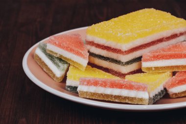 Ahşap arka plandaki tabakta renkli jöle şekeri. Çok renkli marmelatlı reçelli şekerler. Bir yığın üçgen ve dikdörtgen marmelat şekeri.