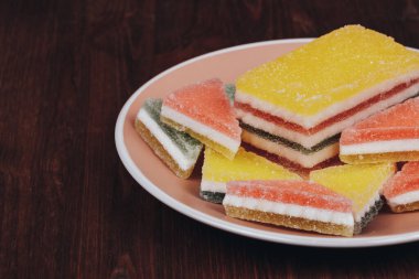 Ahşap arka plandaki tabakta renkli jöle şekeri. Çok renkli marmelatlı reçelli şekerler. Bir yığın üçgen ve dikdörtgen marmelat şekeri.