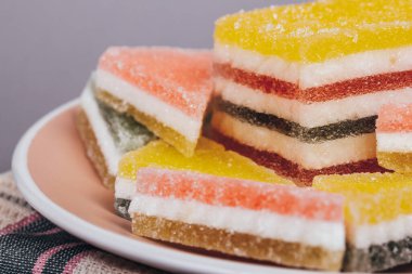 Gri arka planda kareli peçetenin üzerindeki tabakta renkli jöle şekeri. Çok renkli marmelatlı reçelli şekerler. Bir yığın üçgen ve dikdörtgen marmelat şekeri.