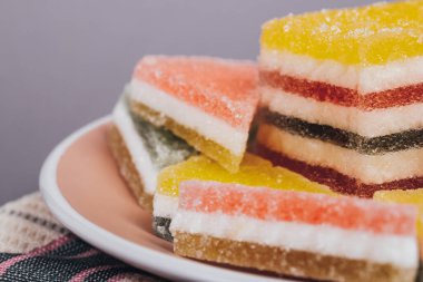 Gri arka planda kareli peçetenin üzerindeki tabakta renkli jöle şekeri. Çok renkli marmelatlı reçelli şekerler. Bir yığın üçgen ve dikdörtgen marmelat şekeri.
