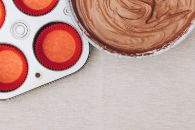 Kakao hamuru kap kekler, kırmızı kağıt kalıplar ve masa örtüsünün üzerindeki metal pişirme tepsisi için. Pişirme işlemi hazırlanıyor. Üst görünüm.