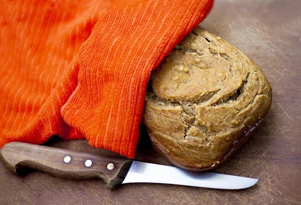 Fresh bread under a napkin and knife — Stock Photo, Image