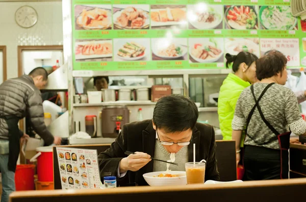 Jeune homme seul manger de la nourriture avec faim à l'intérieur petit et simple restaurant chinois — Photo