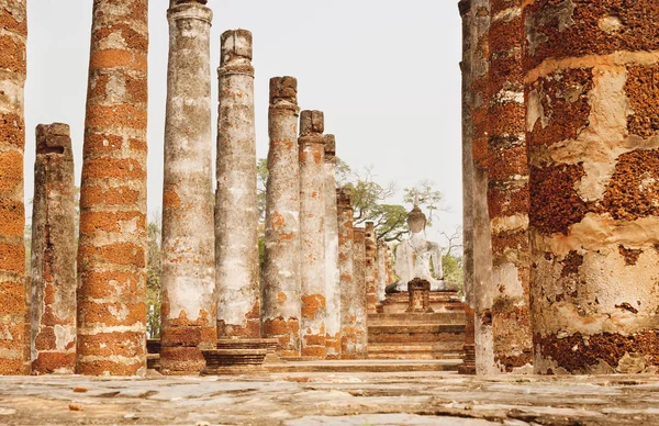 Columnas del antiguo templo en ruinas Wat Maha que con la parte posterior de las estatuas de piedra de Buda en el parque histórico de Sukhothai —  Fotos de Stock