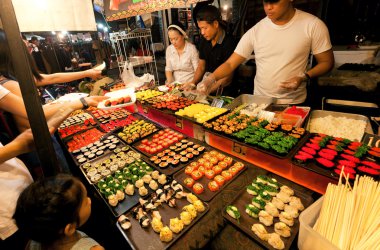 Şehir gece pazarında deniz ürünleri lezzetleri ile Sushi standında seçim yapan insanlar