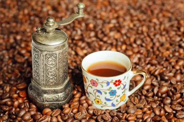 Pequeno moedor de café antigo em uma pilha de grãos de café e uma xícara de café — Fotografia de Stock