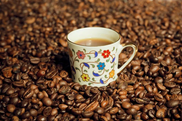 One coffee cup inside the mass of scattered grains of black coffee.