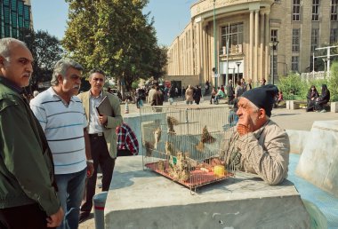 Birdman trades the sparrows on crowded market street of Tehran clipart