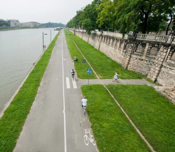 Велосипедисти катаються на набережній вздовж річки Стокове Зображення