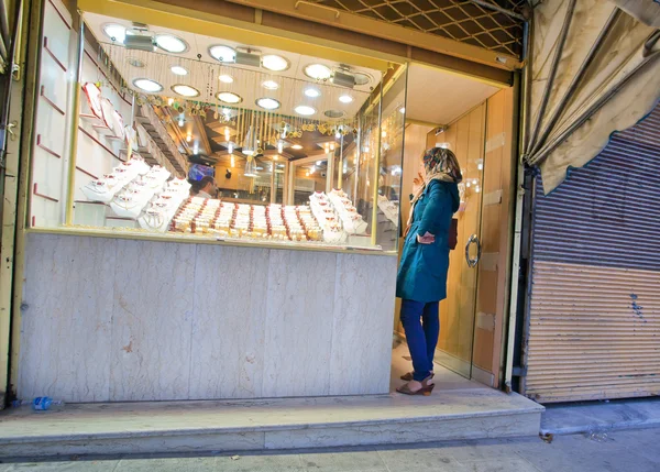 Lonely woman selects gold ornaments in store — Stock Photo, Image