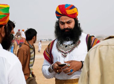 Serious man with a beard and turban dials on a mobile phone