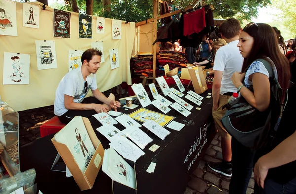 Joven artista dibuja y vende artes gráficas al aire libre — Foto de Stock