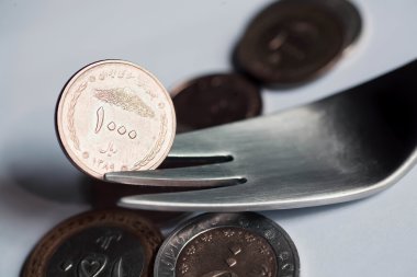 Selective focus on metal fork with iranian currency. clipart
