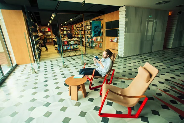 Joven leyendo un libro cerca de la librería dentro de la galería de arte moderno —  Fotos de Stock