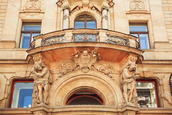 Historical house with balcony in vintage style. Decorative molding and carvings with faces, bodies and sculptures, Prague