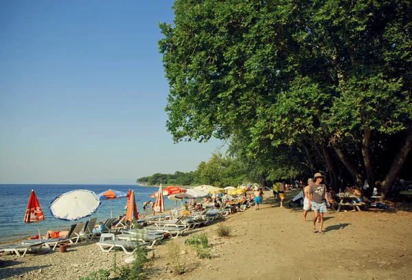 Sunny beach med avslappnade människor, paraplyer och stora gröna träd av turkiska nationalpark — Stockfoto