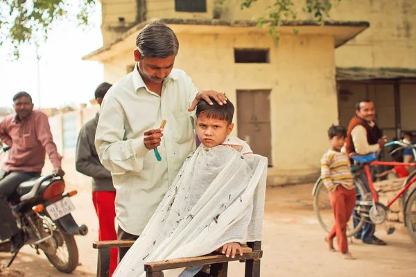 Preschool child with unhappy face doing new hairstyle by village barber — Stock Photo, Image