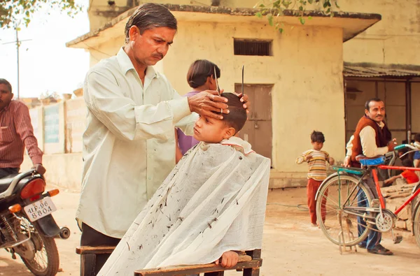 Unidentified boy sitting in chair of rural barber shop and doing new hairstyle by a barber — Stock Photo, Image