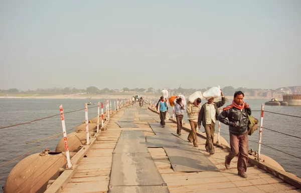 Men carry heavy bags of goods across the bridge over wide river Ganges — ストック写真