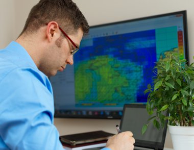 Handsome male meteorologist in glasses on his workplace. clipart