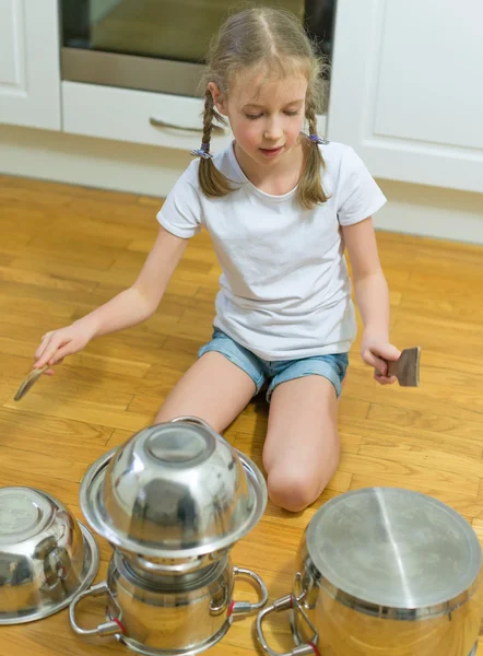 Liten flicka spela trummor på grytor och kastruller i köket. — Stockfoto