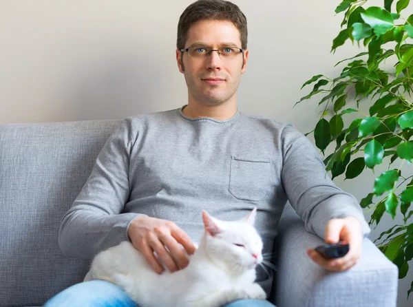 Hombre relajante en el sofá con control remoto de televisión. Ver televisión con su gato . —  Fotos de Stock