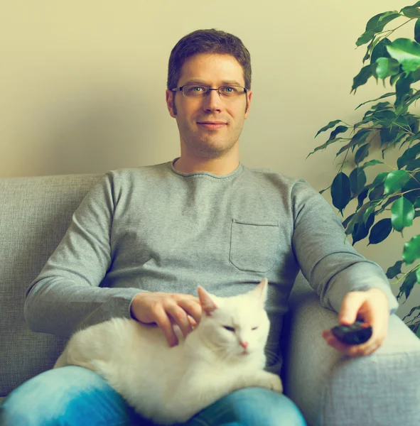 Man relaxing on the sofa with tv remote control. Watching TV with his cat. — Stock Photo, Image