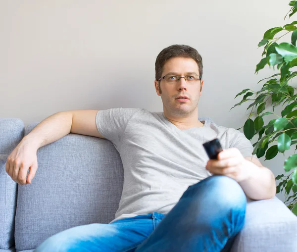 Mann entspannt sich auf dem Sofa mit Fernbedienung. Platz für Text. — Stockfoto