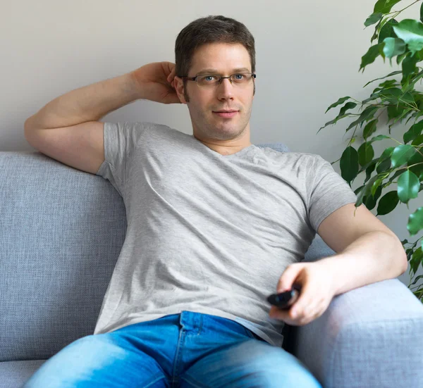 Mann entspannt sich auf dem Sofa mit Fernbedienung. — Stockfoto