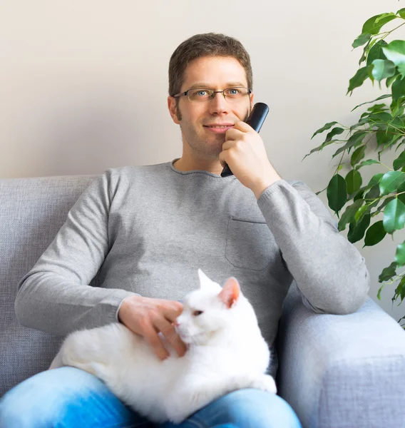 Mann entspannt sich auf dem Sofa mit Fernbedienung. Fernsehen mit seiner Katze. — Stockfoto