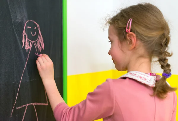 Niedliches kleines Mädchen zeichnet ein Bild auf der Tafel. — Stockfoto