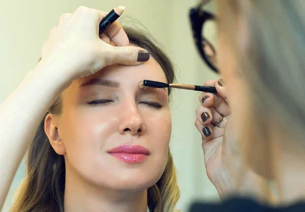 Make-up artist combing eyebrow on model's face. — Stock Photo, Image