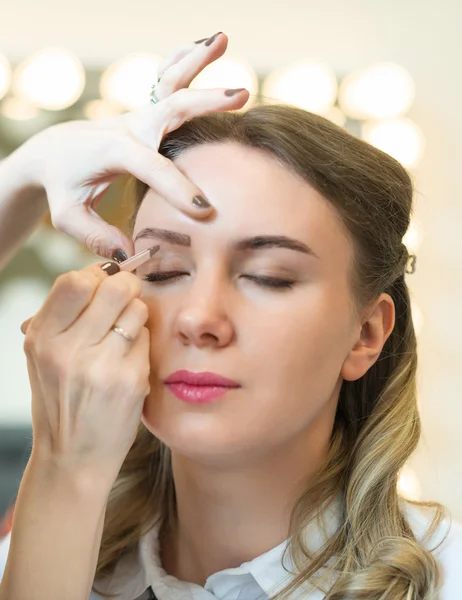 Maquilleuse épilant les sourcils sur le visage du mannequin . — Photo