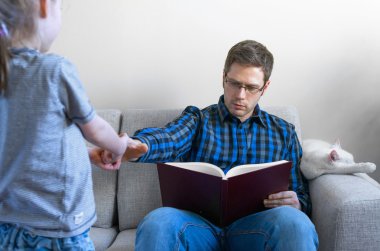 Küçük kız babası kitap okurken rahatsız.