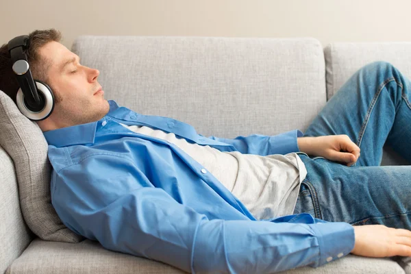 Bonito macho descansando no sofá com fones de ouvido . — Fotografia de Stock