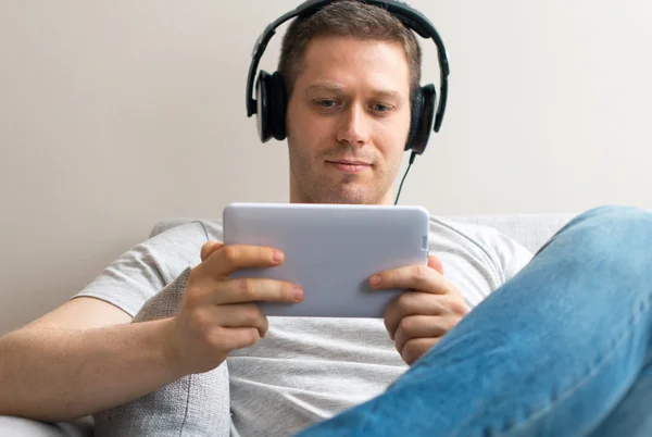 Bonito macho descansando no sofá com tablet pc e fones de ouvido . — Fotografia de Stock