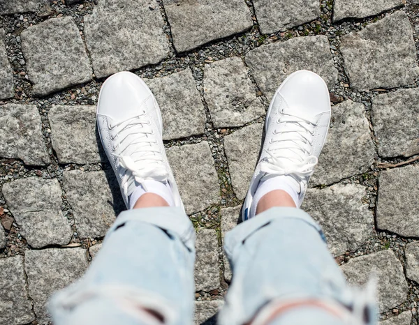 Ben i kvinnliga sneakers på trottoaren. Ovanifrån. — Stockfoto