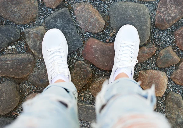 Ben i kvinnliga sneakers på trottoaren. Ovanifrån. — Stockfoto