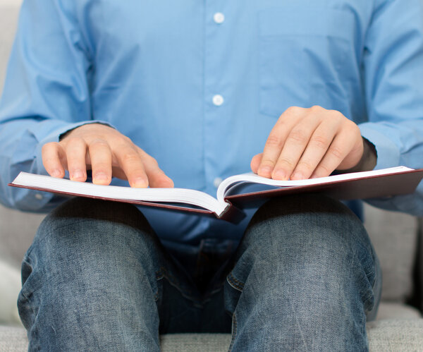 Blind man reading braille book on the couch.