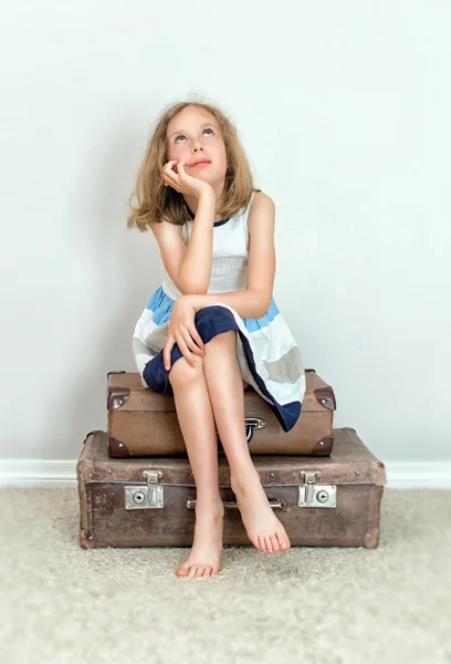 Mała dziewczynka siedzi na walizkach i marzy. — Zdjęcie stockowe