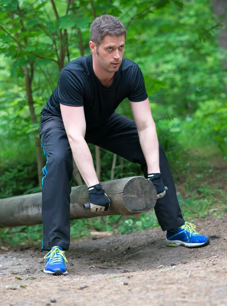 Handsome man lifting log in the forest. — Stock Photo, Image