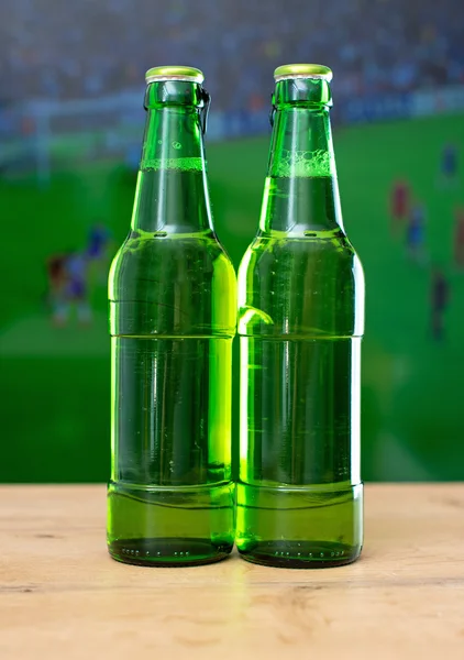 Two bottles of beer in front of TV with football match.